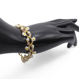 Handmade delicate daisy bracelet featuring white seed bead daisy flowers with yellow centres, white pearls, champagne crystals and gold seed bead accents woven in an open floral chain design with a gold-tone extension clasp, shown worn on a black mannequin hand against a white background.
