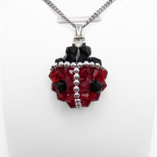 Ladybug-shaped pendant featuring vivid red and black faceted crystals with a silver bead spine and border detailing, black crystal head and a silver-tone bail, displayed on a white stand.