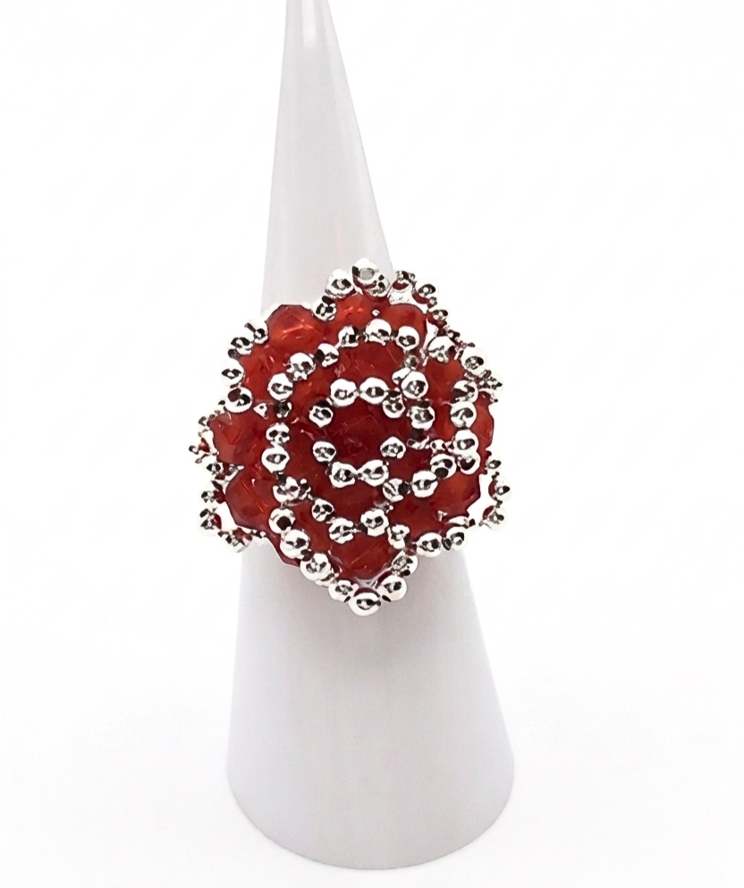 rose-crystal-ring-display Handmade oversized cocktail ring featuring red faceted crystals and silver beads woven in a spiral rose pattern, worn on a finger of a mannequin hand against a white background
