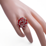 Front view of handmade red crystal and silver beaded cocktail ring with spiral rose design displayed on a white cone ring stand, showing intricate woven bead pattern