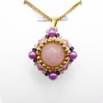 Handmade rose quartz pendant featuring a large smooth round centre stone surrounded by pink crystals, vibrant purple pearls, and gold seed beads in a diamond-shaped silhouette, with a gold-tone bail, shown against a white display stand.