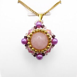 Handmade rose quartz pendant featuring a large smooth round centre stone surrounded by pink crystals, vibrant purple pearls, and gold seed beads in a diamond-shaped silhouette, with a gold-tone bail, shown against a white display stand.