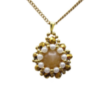 Close-up view of reversible tourmaline pendant featuring a smooth round peach tourmaline centre stone surrounded by white freshwater-style pearls and metallic gold faceted crystals with gold seed bead accents, displayed on a gold-tone curb chain against a white background.