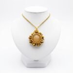 Handmade reversible tourmaline pendant front view featuring a smooth round peach tourmaline centre stone encircled by metallic gold-plated faceted crystals and gold bead accents in a sunburst floral design, with a gold-tone bail, shown on a white display stand.