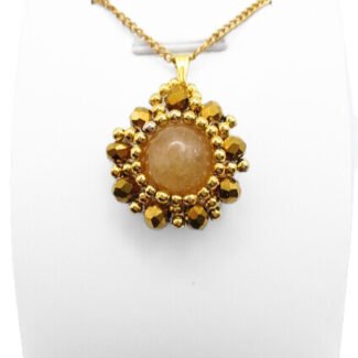 Handmade reversible tourmaline pendant front view featuring a smooth round peach tourmaline centre stone encircled by metallic gold-plated faceted crystals and gold bead accents in a sunburst floral design, with a gold-tone bail, shown on a white display stand.
