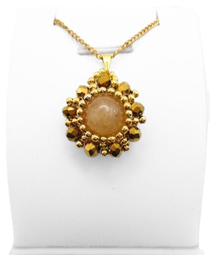 Handmade reversible tourmaline pendant front view featuring a smooth round peach tourmaline centre stone encircled by metallic gold-plated faceted crystals and gold bead accents in a sunburst floral design, with a gold-tone bail, shown on a white display stand.