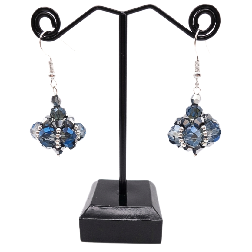 Handmade cluster drop earrings featuring translucent blue and smoky grey crystals, metallic silver crystals with silver seed beads, displayed on a black metal earring stand with silver-toned ear wires.