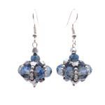 Close-up of handmade drop earrings with translucent blue and smoky-grey faceted crystals and metallic silver crystals woven into a pendulum cluster shape, with silver seed bead accents and silver-toned ear wires, on white background