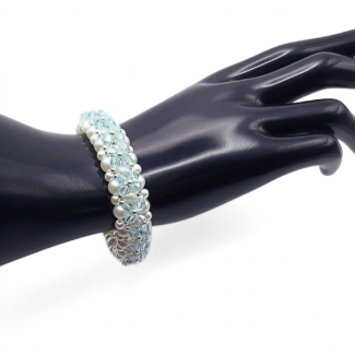 Handmade multi-strand beaded bracelet on a black cone jewellery display stand, photographed against a plain white background. The bracelet is made with white faux pearls and faceted light blue crystal beads arranged in a floral weave with silver bead accents.