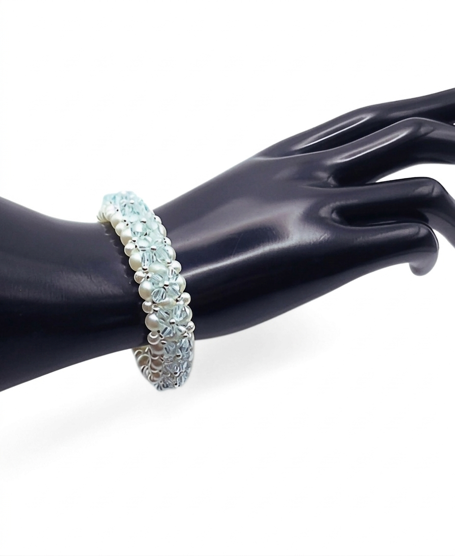 Handmade multi-strand beaded bracelet on a black cone jewellery display stand, photographed against a plain white background. The bracelet is made with white faux pearls and faceted light blue crystal beads arranged in a floral weave with silver bead accents.