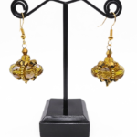 Handmade cluster drop earrings featuring large translucent golden crystals and smaller metallic gold crystals woven into a pendulum cluster shape, with gold bead accents and gold-tone ear wires, displayed on a black metal earring stand.