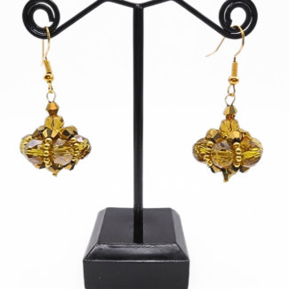Handmade cluster drop earrings featuring large translucent golden crystals and smaller metallic gold crystals woven into a pendulum cluster shape, with gold bead accents and gold-tone ear wires, displayed on a black metal earring stand.