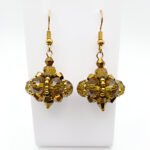 Close-up of handmade golden crystal drop earrings with large faceted translucent gold crystals and smaller metallic gold crystals in a pendulum cluster formation, finished with gold accent beads and gold-tone ear wires, on a white jewellery display.