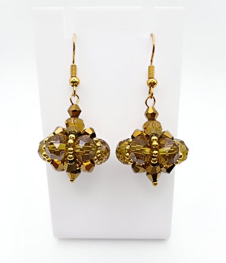 Close-up of handmade golden crystal drop earrings with large faceted translucent gold crystals and smaller metallic gold crystals in a pendulum cluster formation, finished with gold accent beads and gold-tone ear wires, on a white jewellery display.