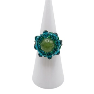 Handmade beaded cocktail ring featuring an olive green tourmaline centre stone surrounded by teal blue and emerald green crystal beads, displayed on a white cone ring stand