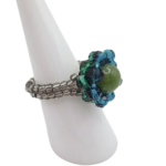 Side view of handmade beaded ring showing silver seed bead band construction and layered teal blue and green crystal halo surrounding an olive green tourmaline centre stone