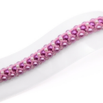 Wide bracelet featuring deep purple and lavender pearls woven together with small white pearl accents, bright pink beads and light pink crystal detailing in a repeating diagonal pattern, with a gold-tone lobster clasp, displayed flat on a white jewellery stand against a white background.