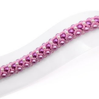 Wide bracelet featuring deep purple and lavender pearls woven together with small white pearl accents, bright pink beads and light pink crystal detailing in a repeating diagonal pattern, with a gold-tone lobster clasp, displayed flat on a white jewellery stand against a white background.