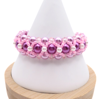 Handmade wide purple and pink pearl bracelet featuring deep purple and lavender pearls, small white pearl accents and bright pink beads and light pink crystal detailing in a full rounded woven design, displayed on a white cone bracelet stand with a wooden base against a white background.