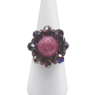 Handmade beaded cocktail ring featuring a round rose pink tourmaline centre stone surrounded by faceted purple AB crystal beads in a floral halo design, displayed on a white cone ring stand