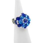 Side view of a handmade sapphire blue and aquamarine crystal cluster cocktail ring with silver-tone beaded band, displayed on a white ring cone