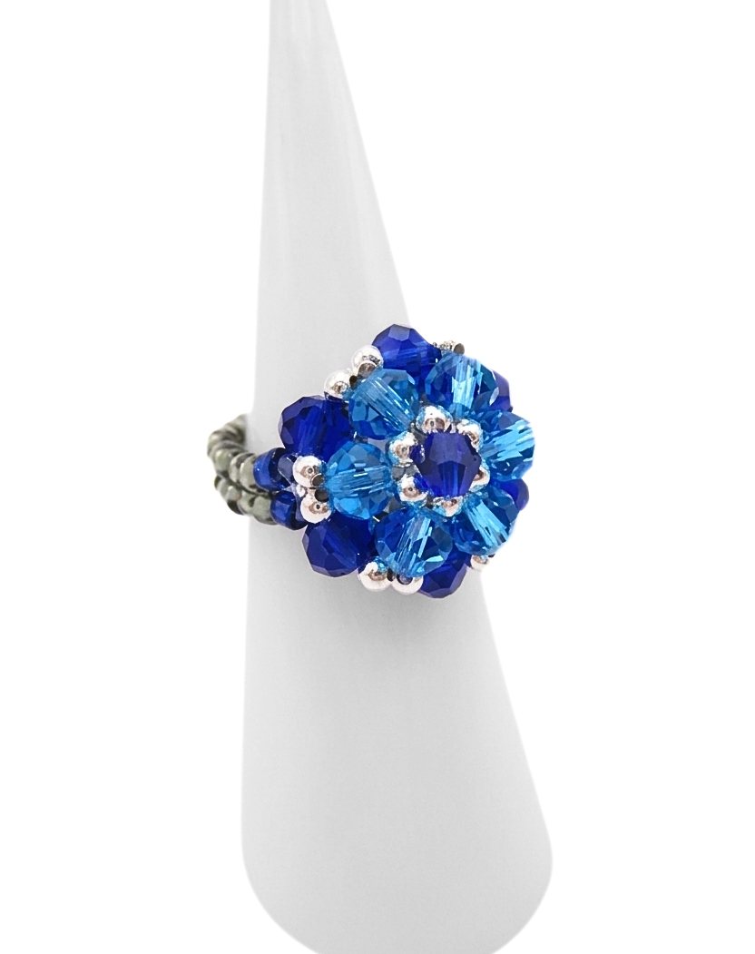 Side view of a handmade sapphire blue and aquamarine crystal cluster cocktail ring with silver-tone beaded band, displayed on a white ring cone