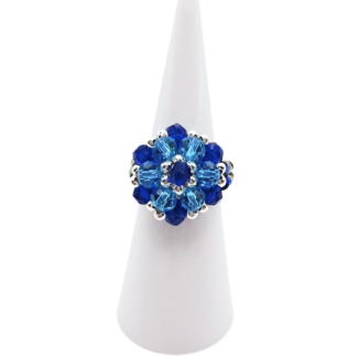 Handmade crystal cluster ring featuring sapphire blue and aquamarine crystals with silver-tone accents, displayed on a white cone ring stand - front view