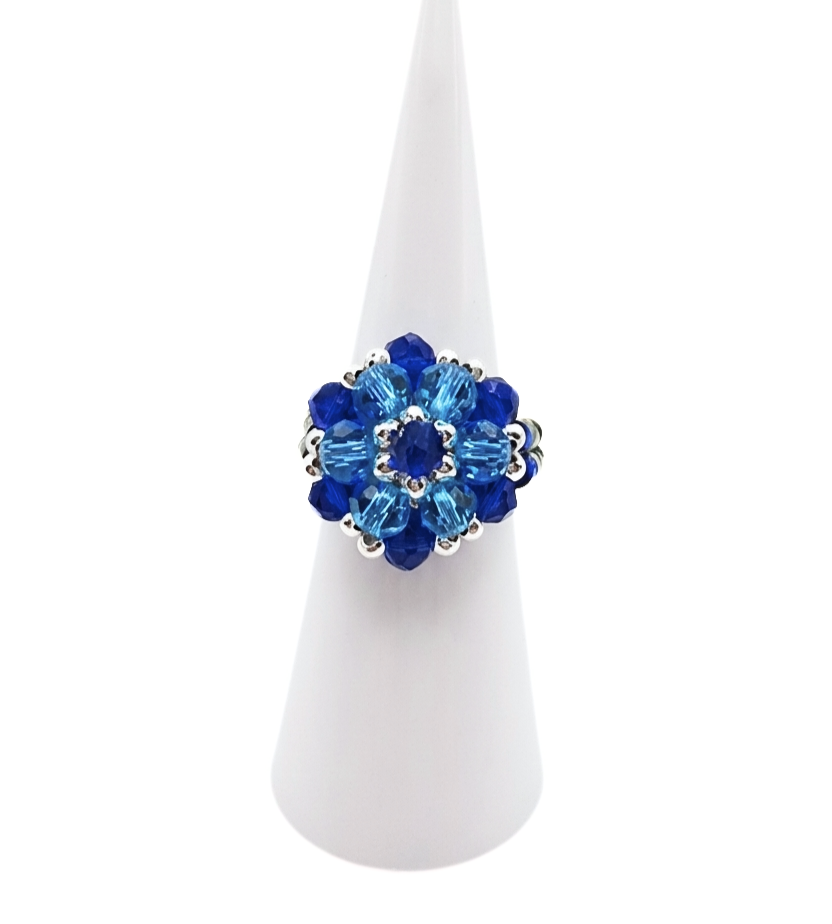 Handmade crystal cluster ring featuring sapphire blue and aquamarine crystals with silver-tone accents, displayed on a white cone ring stand - front view