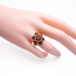 Handmade rose-pink tourmaline and burgundy crystal flower ring with gold bead halo worn on mannequin hand, showing ring size and scale