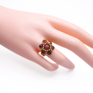 Handmade rose-pink tourmaline and burgundy crystal flower ring with gold bead halo worn on mannequin hand, showing ring size and scale