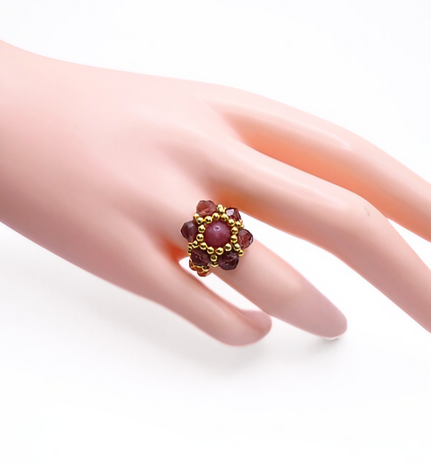 tourmaline-ring-hand-display Handmade rose-pink tourmaline and burgundy crystal flower ring with gold bead halo worn on mannequin hand, showing ring size and scale
