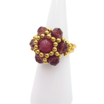 Angled side view of handmade pink tourmaline beaded ring with burgundy crystal petals and gold bead halo on gold seed bead band, displayed on white ceramic ring cone