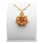 Handmade peach and champagne crystal statement pendant featuring a large faceted peach centre crystal surrounded by champagne crystals and gold coloured beads on a gold-tone chain, displayed on a white jewellery stand.