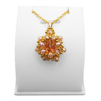 Handmade peach and champagne crystal statement pendant featuring a large faceted peach centre crystal surrounded by champagne crystals and gold coloured beads on a gold-tone chain, displayed on a white jewellery stand.