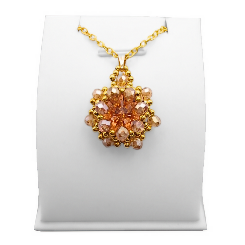 Handmade peach and champagne crystal statement pendant featuring a large faceted peach centre crystal surrounded by champagne crystals and gold coloured beads on a gold-tone chain, displayed on a white jewellery stand.