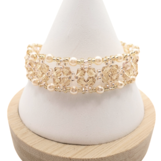 Handmade crystal bracelet featuring champagne faceted crystals and lustrous champagne pearls woven together with gold bead accents in an open lattice diamond pattern, displayed on a white cone bracelet stand with a wooden base against a white background.