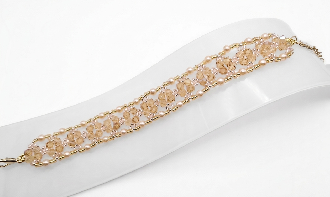 Handmade champagne crystal bracelet featuring faceted crystals and small champagne pearls woven with gold bead accents in an open lattice diamond pattern, displayed flat on a white jewellery stand showing full length and gold-tone lobster clasp with extension chain against a white background.
