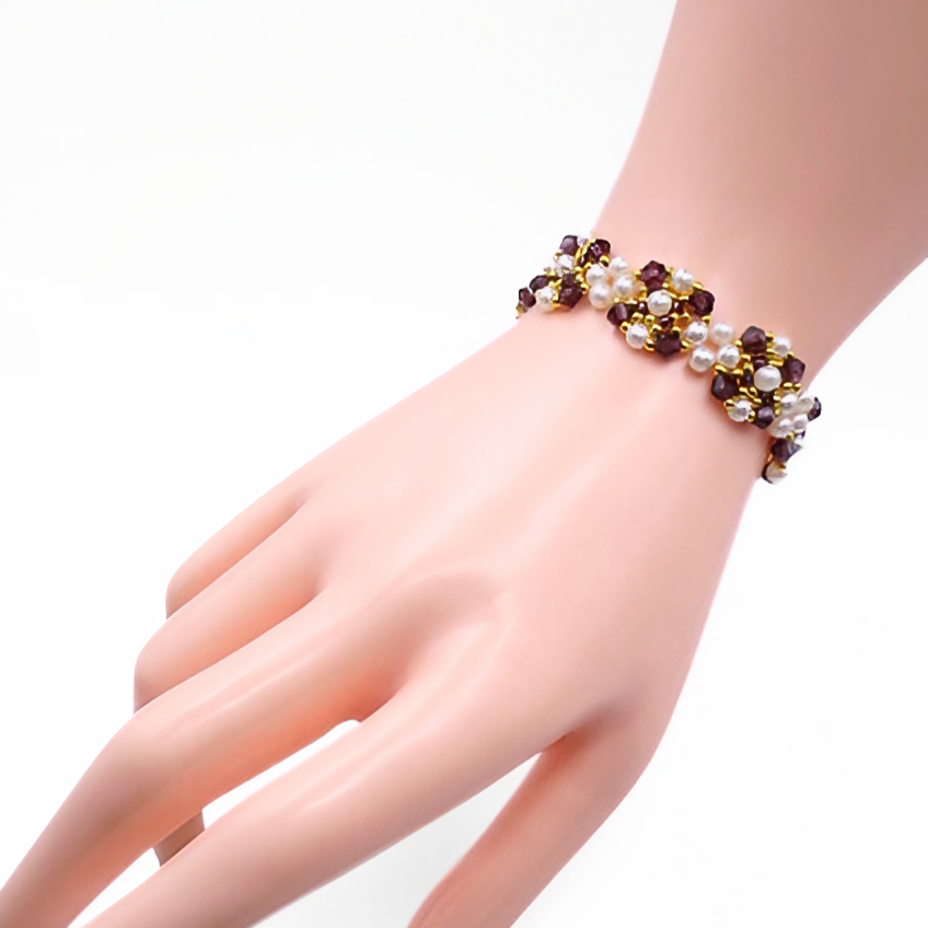 Handmade purple crystal and white pearl bracelet with gold bead accents in a repeating weave pattern, shown worn on a mannequin wrist and hand against a white background.