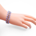 Handmade wide blue and grey crystal bracelet featuring alternating light blue and metallic grey faceted crystals in a repeating diamond lattice weave with clear seed bead accents, shown worn on a mannequin wrist against a white background.