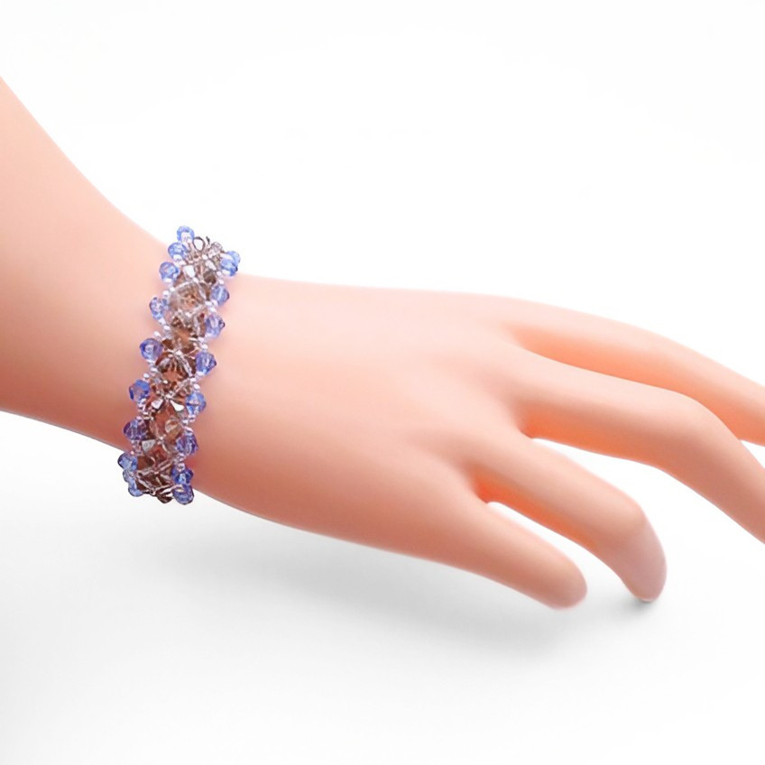 Handmade wide blue and grey crystal bracelet featuring alternating light blue and metallic grey faceted crystals in a repeating diamond lattice weave with clear seed bead accents, shown worn on a mannequin wrist against a white background.