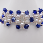 Close-up view of the handmade wide bracelet featuring deep metallic-blue AB reflective faceted crystals and lustrous white pearls woven together in a repeating floral-cluster pattern with silver-tone bead accents, shown against a white cone bracelet stand.