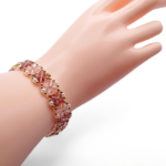 Handmade pink and purple crystal bracelet featuring light pink and purple faceted crystals in a repeating four-petal flower pattern with white pearl and gold seed bead accents, shown worn on a mannequin wrist and hand against a white background.