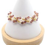 Handmade bracelet featuring purple faceted crystals and lustrous white pearls woven together in a zigzag pattern with gold seed bead accents throughout, displayed on a white cone bracelet stand with a wooden base against a white background.