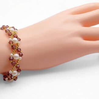 Handmade purple crystal and white pearl bracelet with gold bead accents in a delicate zigzag weave pattern, shown worn on a mannequin wrist and hand against a white background.