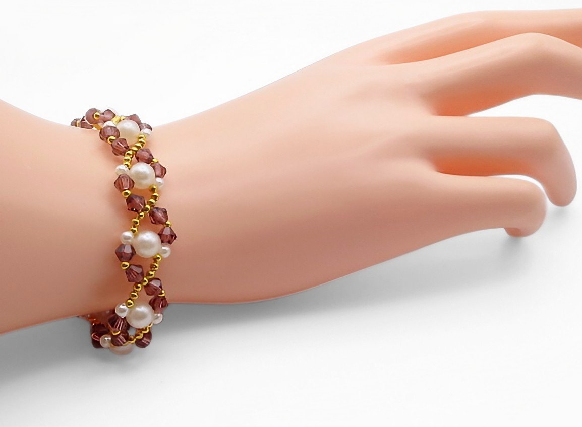Handmade purple crystal and white pearl bracelet with gold bead accents in a delicate zigzag weave pattern, shown worn on a mannequin wrist and hand against a white background.