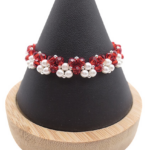 Handmade red crystal and white pearl bracelet featuring vivid red faceted crystals and lustrous white pearls woven in a bold repeating cluster pattern with silver-tone bead accents, displayed on a black cone bracelet stand with a wooden base against a white background.