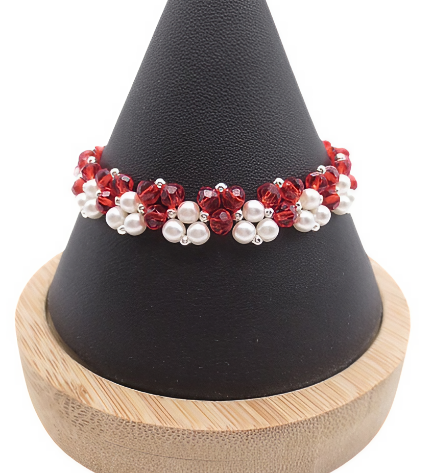 red-crystal-pearl-bracelet-cone-display Handmade red crystal and white pearl bracelet featuring vivid red faceted crystals and lustrous white pearls woven in a bold repeating cluster pattern with silver-tone bead accents, displayed on a black cone bracelet stand with a wooden base against a white background.