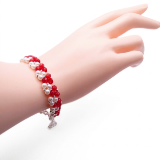 Handmade bracelet featuring vivid red faceted crystals and lustrous white pearls woven together in a repeating cluster pattern with silver-tone bead accent, shown worn on a mannequin wrist and hand against a white background.