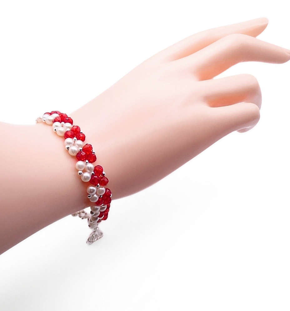 red-crystal-pearl-bracelet-wrist-display Handmade bracelet featuring vivid red faceted crystals and lustrous white pearls woven together in a repeating cluster pattern with silver-tone bead accent, shown worn on a mannequin wrist and hand against a white background.