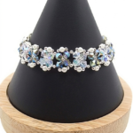 Handmade bracelet featuring iridescent opal and silvery grey aurora borealis AB finish faceted crystals and small white pearls woven together in a repeating floral cluster pattern with silver-tone bead accents, shown worn on a black mannequin hand and wrist against a white background.